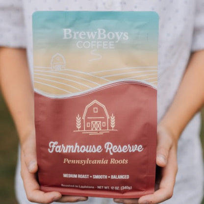 Hands holding a bag of BrewBoys Farmhouse Reserve medium roast coffee outdoors