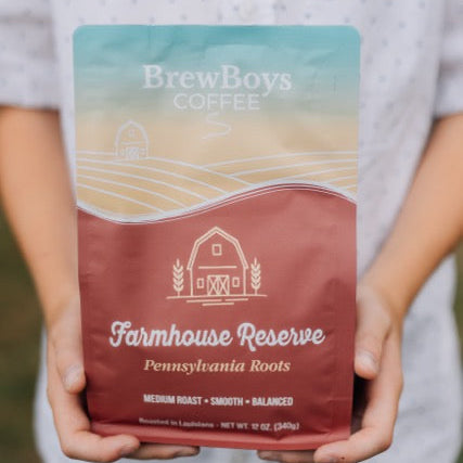 Hands holding a bag of BrewBoys Farmhouse Reserve medium roast coffee outdoors
